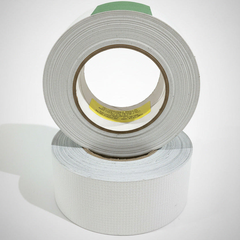 E&H 753-MP two rolls stacked — yellow BMS 5-157 core label and green flag visible, dull gray PEEK scrim surface